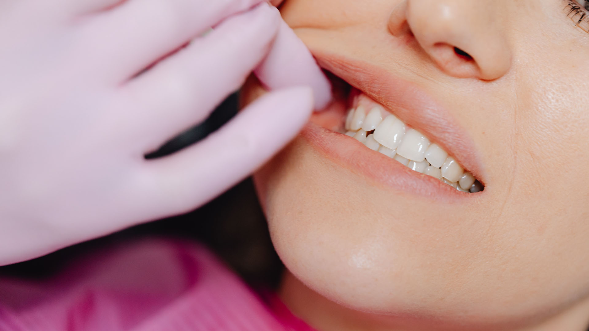 A dentist in pink latex gloves examining a patient's white teeth during a dental check-up.