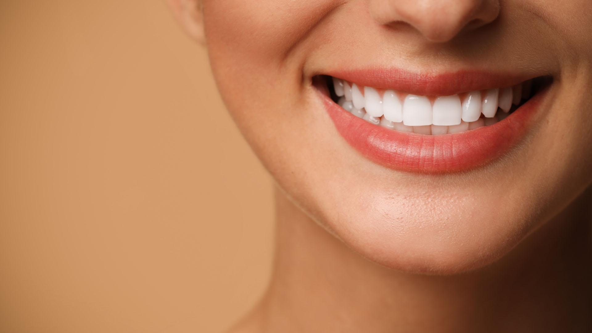 Close-up of a woman smiling with bright white teeth and red lips against a warm beige background