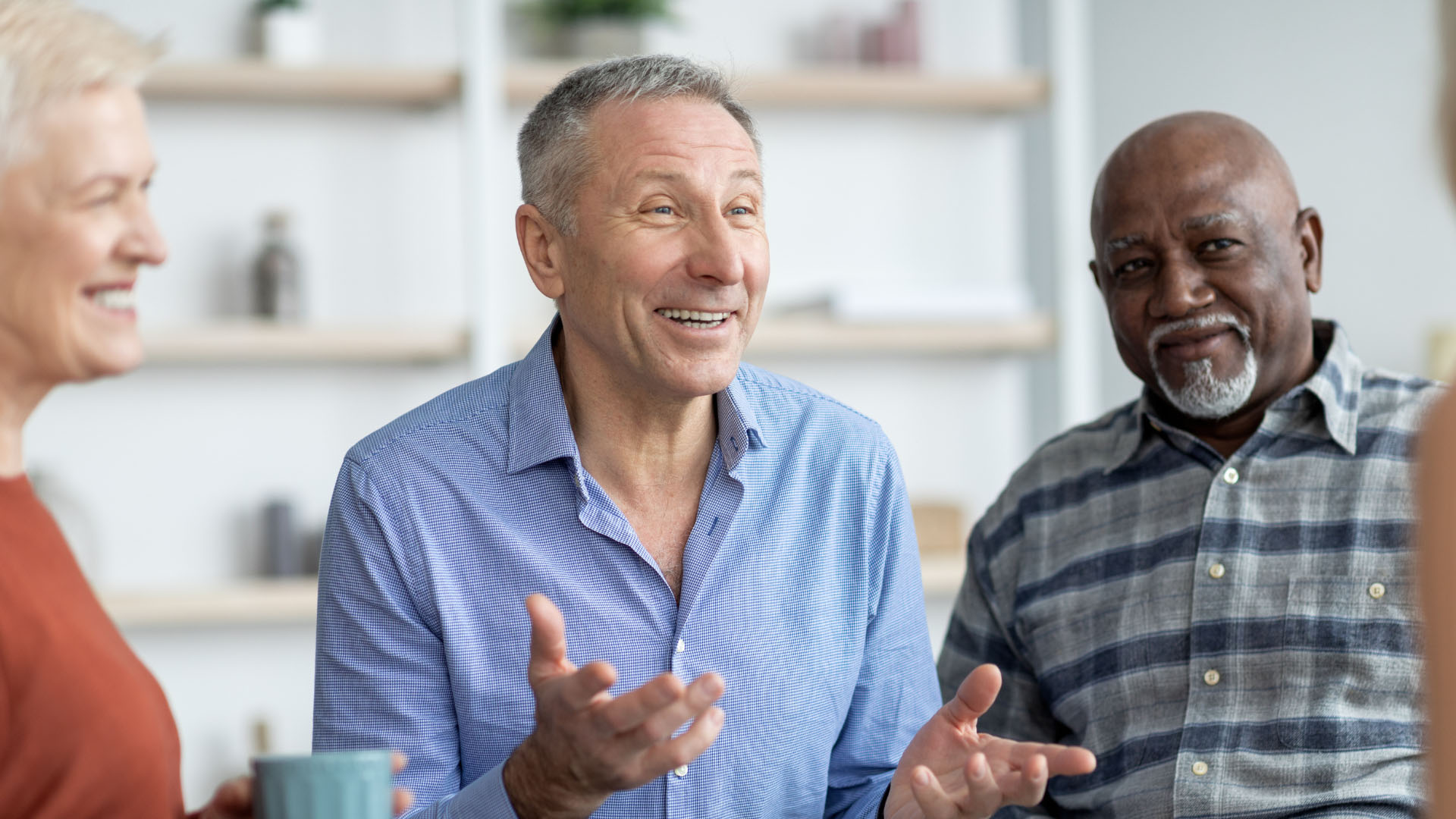 A group of older adults chatting and smiling together in a relaxed social setting.