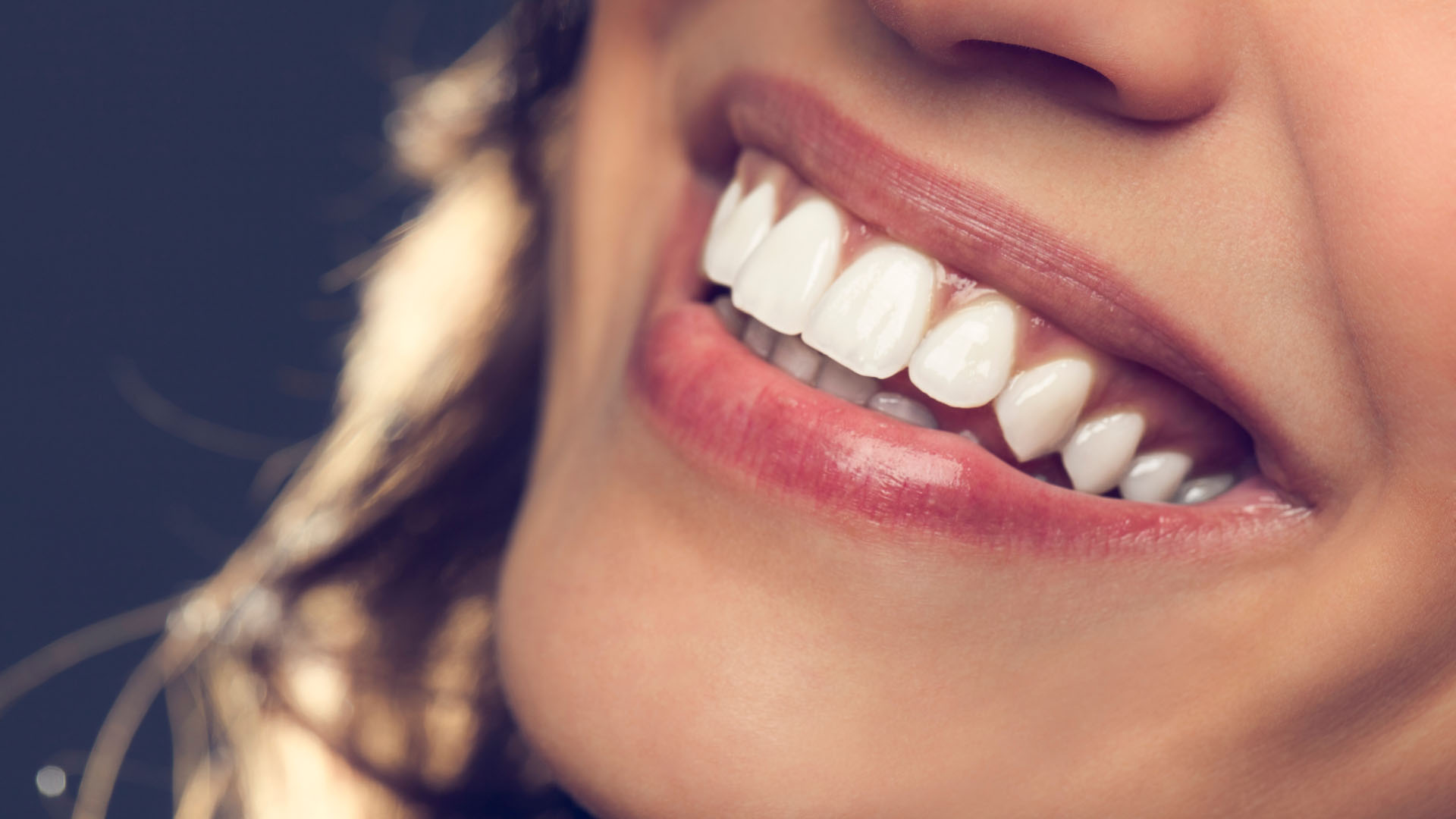 Close-up of a woman smiling with bright, white teeth against a dark background