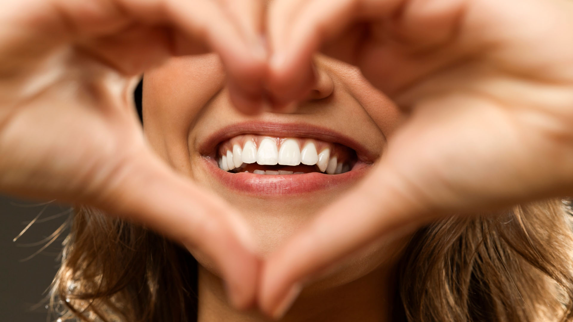 Woman forming a heart shape with her hands, framing her bright white smile and healthy teeth