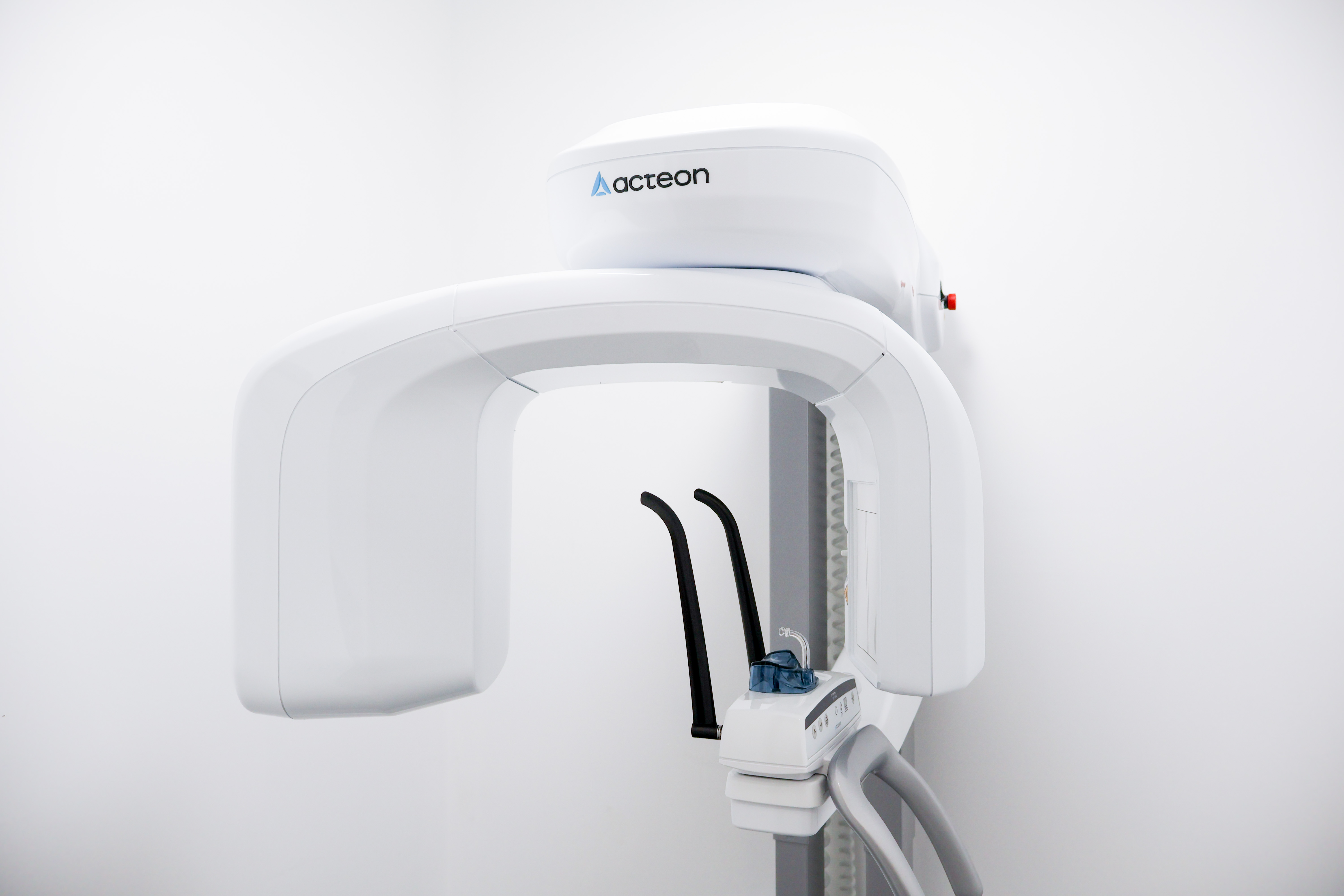 Acteon dental X-ray machine mounted on a wall, featuring a white U-shaped rotating arm and patient positioning guides