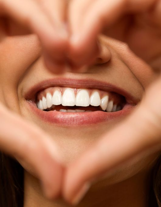 Woman forming a heart shape with her hands, framing her bright smile and white teeth