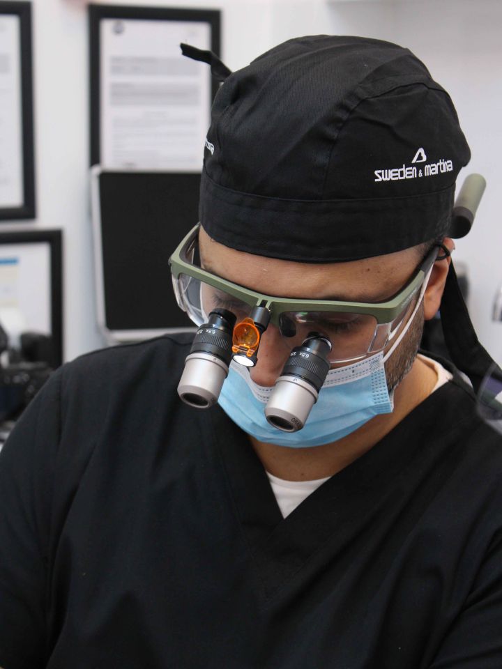Dental professional wearing magnification loupes and a surgical face mask focused during a procedure