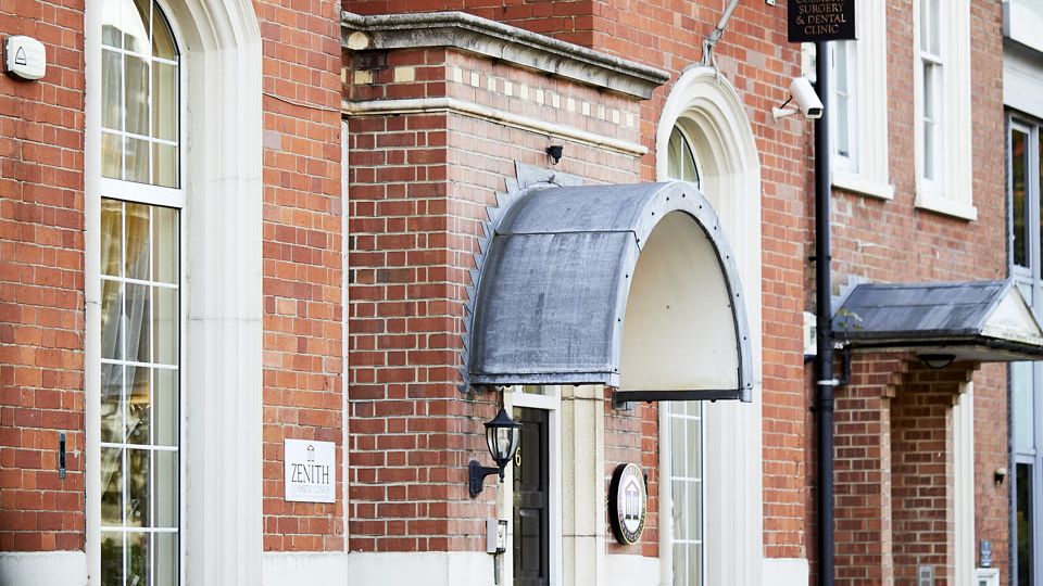 Red brick Zenith clinic building entrance with an arched metal canopy and outdoor lighting.