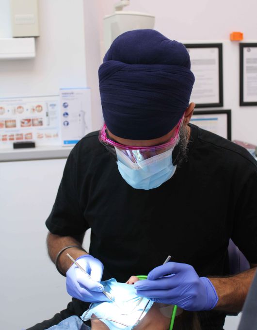 A dentist wearing a blue turban, face mask, and gloves performing a dental procedure on a patient in a clinic.