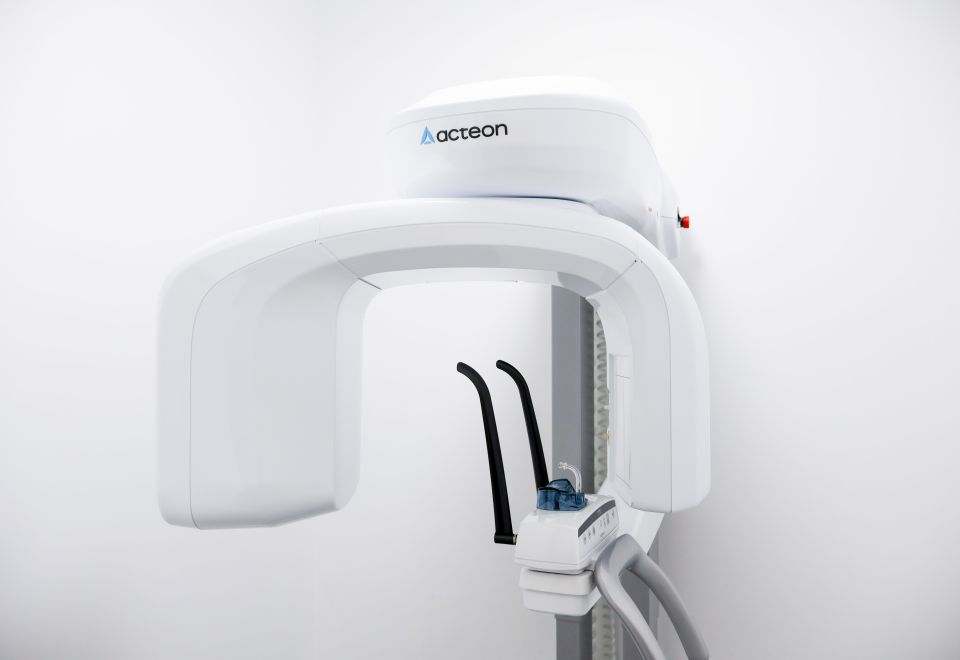 Acteon dental X-ray machine mounted on a wall, featuring a white U-shaped rotating arm and patient positioning guides