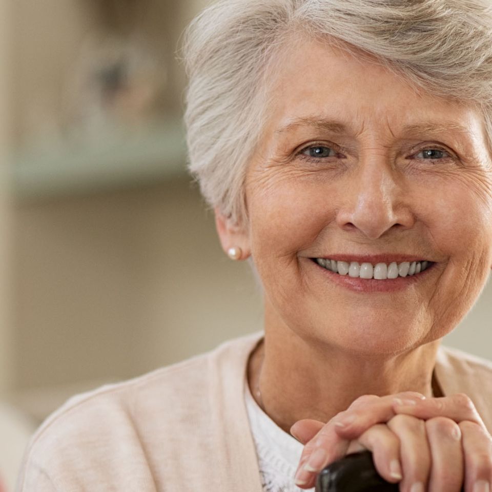 Smiling middle-aged man with grey-streaked hair, round glasses and a light blue shirt against a grey background